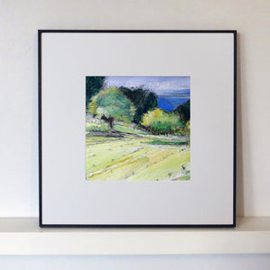 Framed painting of a landscape with trees and fields on a white wall.