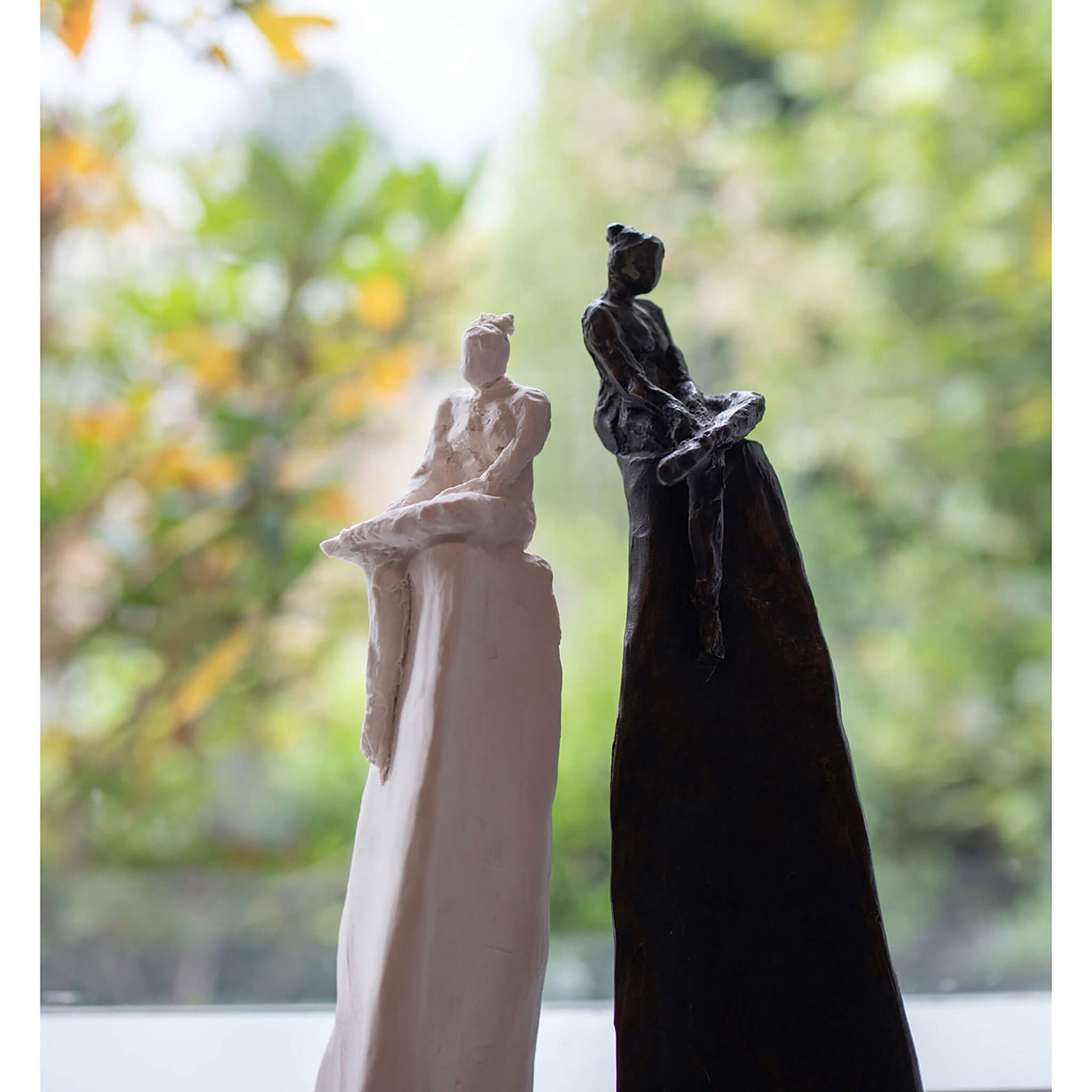 Two small human figure sculptures by Gillian Brett, one white and one black.