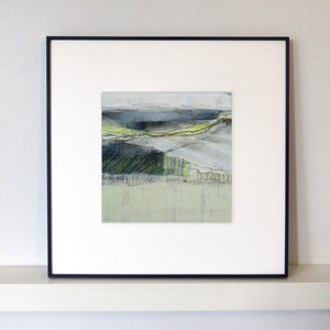 Framed abstract landscape art print with a white mat and a thin black frame, displayed on a white shelf against a light gray wall.