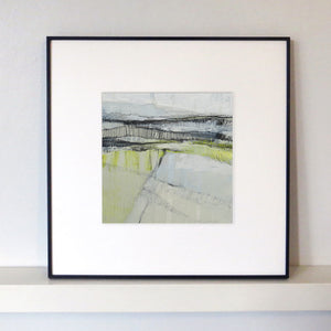 Framed abstract landscape art print with a white mat and black frame, displayed on a white shelf against a light gray wall.