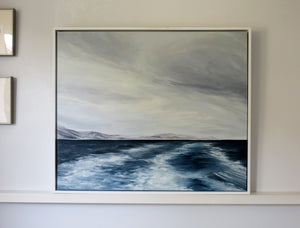 Framed abstract painting of a landscape with mountains and water on a wall.