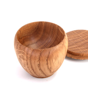 A small round wooden bowl with a matching wooden lid resting behind it on a white background.