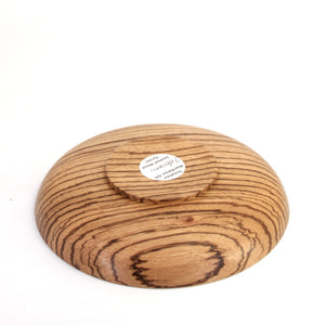 A round wooden serving bowl shown from the bottom side, featuring a prominent natural wood grain pattern with dark brown streaks on a light tan wood base. 
