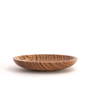 A shallow round wooden bowl with a prominent dark brown and tan wood grain pattern, photographed on a seamless white background.